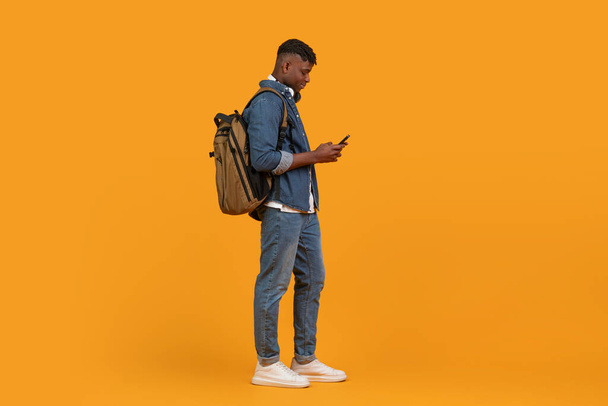 Afro-americano proyecta un ambiente multiétnico mientras revisa casualmente su teléfono, aislado sobre fondo naranja - Foto, Imagen