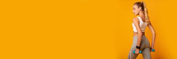 Sportos nő pózol Dumbbells felett sárga stúdió háttér. Edzés koncepció. Fénymásolási tér, Panoráma - Fotó, kép