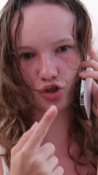 A woman talks on the phone, ordering delivery, communicates with friends, uses social networks and the Internet. Relaxing on beach emotions of young girl burnt skin red cheeks wet hair. - Footage, Video