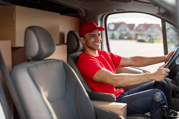 Χαμογελώντας Ευρωπαίος ταχυδρόμος κάθεται στο αυτοκίνητο ως οδηγός, παράδοση δεμάτων στους πελάτες - Φωτογραφία, εικόνα