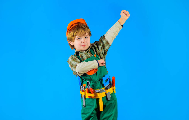 Pequeno construtor em capacete de construção e cinto de ferramentas. Kid reparador em chapéu duro e macacão com cinto de ferramentas de ferramentas de brinquedo para a construção. Sorrindo menino em uniforme com conjunto de ferramentas de construção de brinquedos - Foto, Imagem