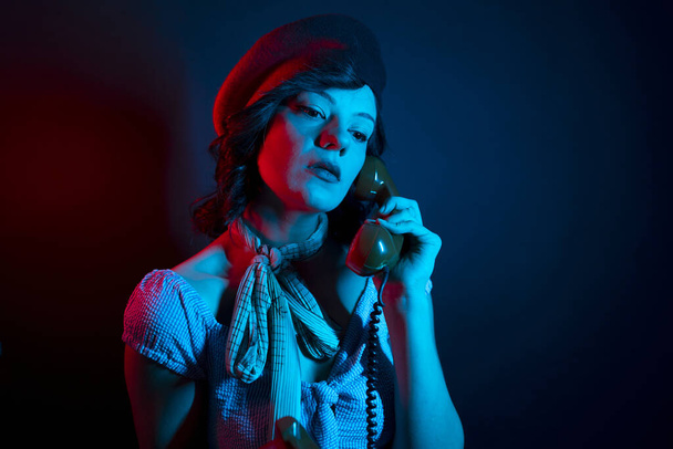 Jonge vrouw in gesprek met Orange Retro Phone. High Fashion model vrouw in kleurrijke heldere neon blauw en paars lichten poseren in studio. - Foto, afbeelding