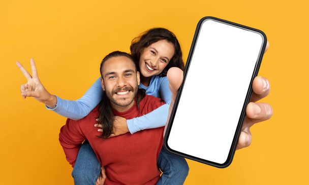 Um homem e uma mulher alegres estão brincando interagindo uns com os outros, com o homem segurando um smartphone que tem uma tela em branco adequada para o modelo digital - Foto, Imagem