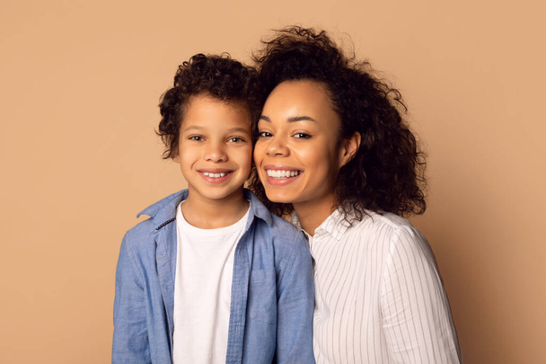 Mujer afroamericana y un niño están de pie juntos, sonriendo y posando para una cámara. La mujer tiene su brazo alrededor del niño, ambos mirando directamente a la cámara. - Foto, imagen