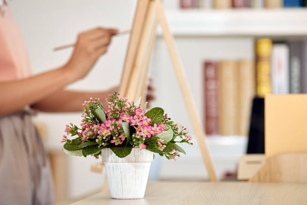 Κοντινό πλάνο του χεριού του καλλιτέχνη απαλά ζωγραφική καμβά, εμπνευσμένο από όμορφο ροζ λουλούδια διάταξη σε λευκό δοχείο ως πρώτο πλάνο - Φωτογραφία, εικόνα