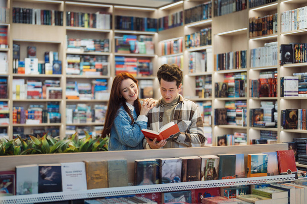 Neşeli genç bir çift, geniş bir edebiyat koleksiyonu ile çevrili, iyi düzenlenmiş bir kütüphanede kitaplara bakarken keyifli bir anı paylaşıyor.. - Fotoğraf, Görsel