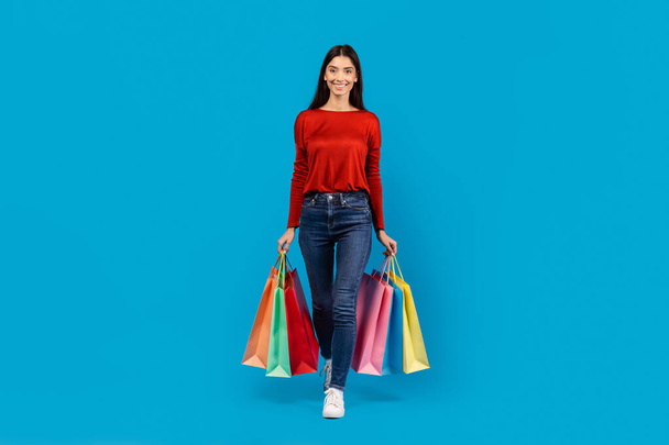 Une femme portant un pull rouge debout tout en tenant des sacs à provisions dans ses mains. Elle semble être à l'extérieur, peut-être après un voyage de shopping. - Photo, image