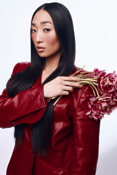 Elegante donna asiatica in giacca di pelle rossa con mazzo di fiori in ambiente urbano - Foto, immagini