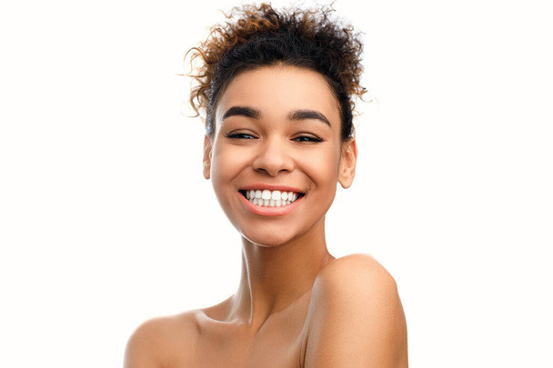 Işıl ışıl gülümseyen, sıcak, kendine güveni ve mutluluğu olan, beyaz bir arka planda soyutlanmış genç bir Afrikalı Amerikalı kadının yakın plan fotoğrafı. - Fotoğraf, Görsel