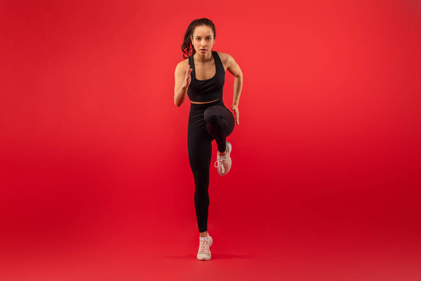 Uma mulher vestindo um top de sutiã esportivo preto e leggings é mostrado exercendo. Ela está envolvida em atividade física, demonstrando aptidão e força em sua roupa de treino. - Foto, Imagem