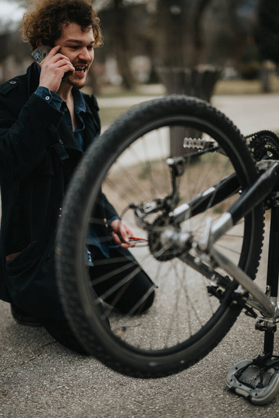 Een jonge zakenman neemt een pauze om zijn fiets te repareren in het park, het demonstreren van probleemoplossend vermogen. - Foto, afbeelding