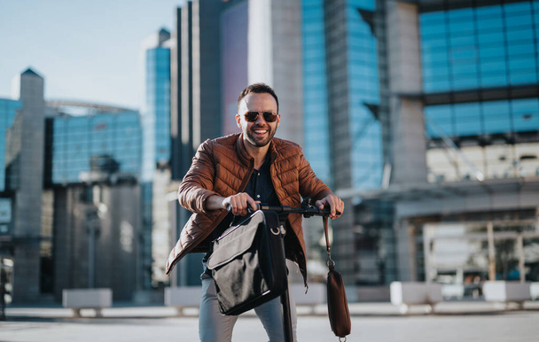 都市設定で電動スクーターに乗って,ブリーフケースを運ぶ自信のある男性ビジネスマン. - 写真・画像