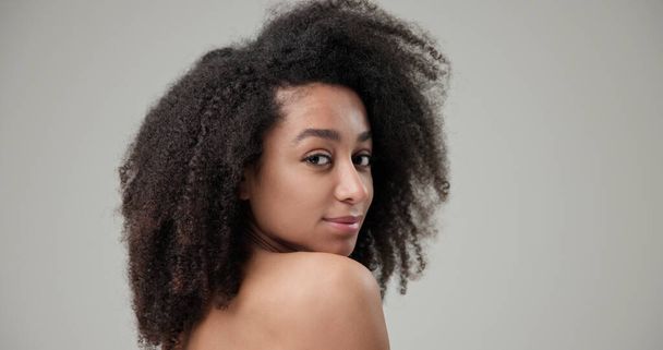 Beauty and Healthcare concept - Beautiful African American woman with curly afro hairstyle hair and clean, healthy skin on gray studio background posing and looking at camera. High quality photo - Fotografie, Obrázek
