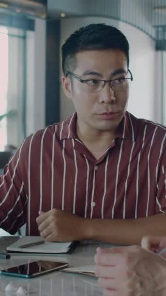 Asyalı işadamının ofiste müşteriyle finansal projenin detaylarını tartışırken dikey çekimi - Video, Çekim