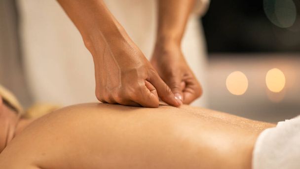 Eine Frau liegt mit dem Gesicht nach unten auf einem Massagetisch in einem Wellnessbereich, während eine Massagetherapeutin eine Rückenmassage durchführt. Die Hände der Therapeuten sind sichtbar, wenn sie Druck ausüben, Nahaufnahme - Foto, Bild