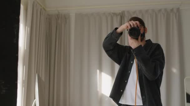 Közepes lövés képzett kaukázusi férfi fotós segítségével professzionális dslr kamera, miközben fotózás modell napsütötte minimalista stúdió és így ajánlásait pózol - Felvétel, videó