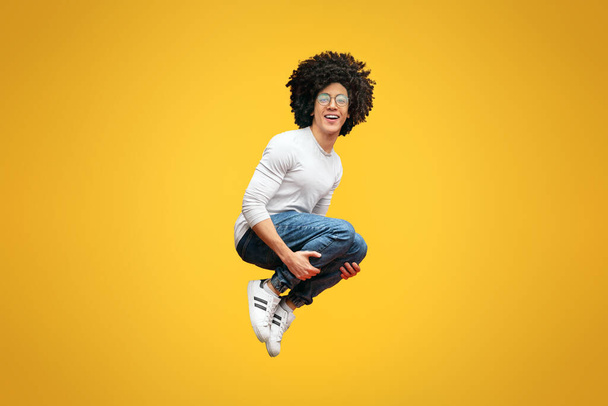 Cheerful millennial man jumping in bomb style, orange studio background - Photo, Image
