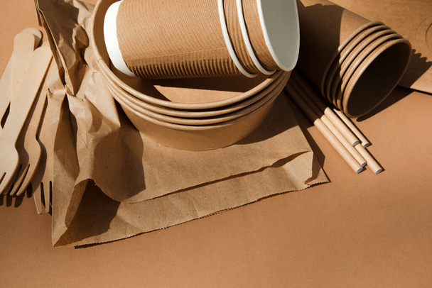Een set van papieren gebruiksvoorwerpen en houten bestek op een bruine achtergrond. Milieuvriendelijk, afvalvrij concept. Bovenaanzicht - Foto, afbeelding