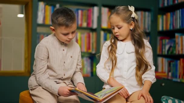 κοντά σε ένα βιβλιοπωλείο στην περιοχή των παιδιών ένα όμορφο αγοράκι με ελαφρά ρούχα και ένα κορίτσι διαβάζει ένα βιβλίο - Πλάνα, βίντεο