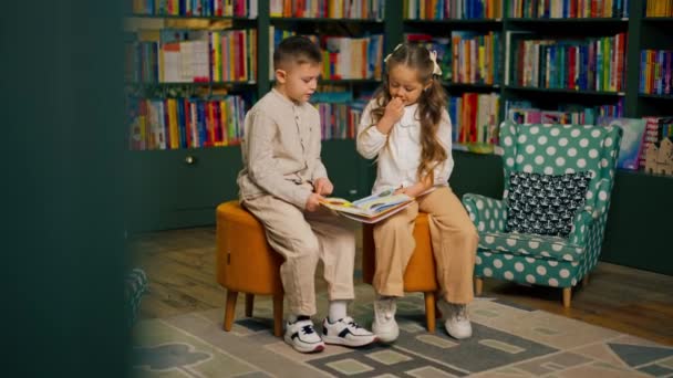 в книжном магазине в детской зоне красивый маленький мальчик в легкой одежде и девочка читает одну книгу - Кадры, видео