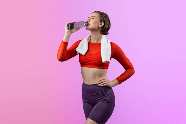 Vücut uzunluğunun tamamı atletik ve sportif genç bir kadını havluyla ve içme suyuyla izole edilmiş arka planda egzersiz yaparken çekilir. Sağlıklı aktif ve vücut bakımı yaşam tarzı. - Fotoğraf, Görsel