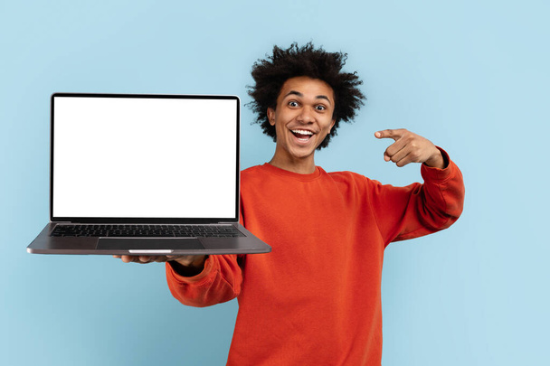 Hevesli bir Afrikalı Amerikalı dizüstü bilgisayar sunuyor, mavi ekranda izole edilmiş, modeller ve reklam alanları için mükemmel. - Fotoğraf, Görsel