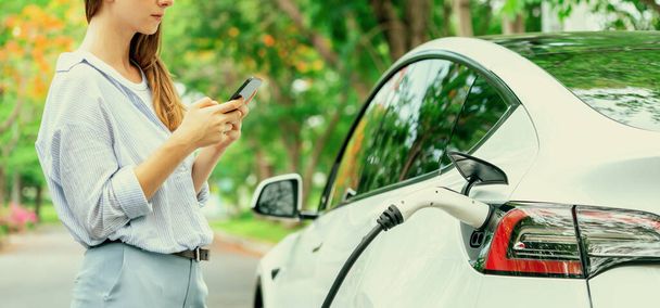 Panorama banner woman use smartphone online banking application to pay for EV car battery charging from EV charging station during autumn vacation holiday trip at national park or forest. Exalt - Photo, Image
