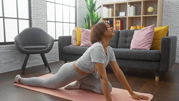 Afroamerykanka rozciągająca się na macie do jogi w nowoczesnym salonie, ucieleśniająca wellness i zdrowy styl życia. - Zdjęcie, obraz