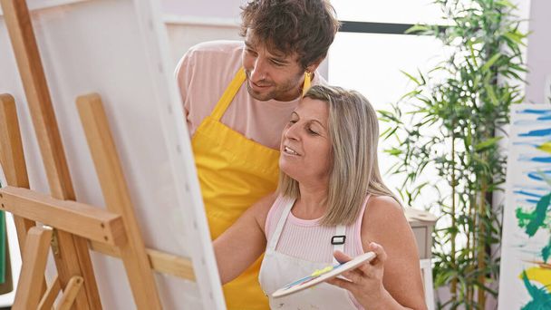 Dva sebevědomí umělci, muž a žena, si užívají kreslení s úsměvy v interiérovém ateliéru, zatímco se učí a malují - Fotografie, Obrázek