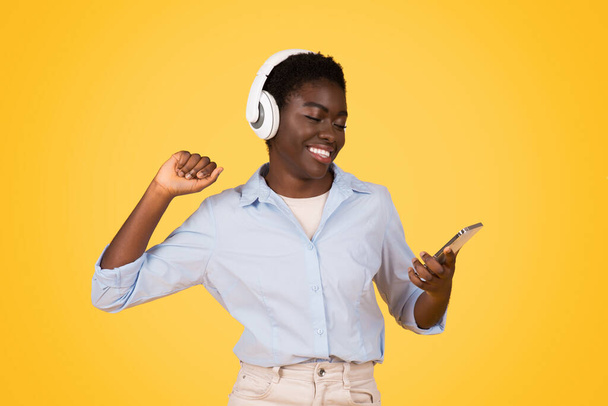 Яркий образ африканской американки, скорее всего зумер, наслаждающейся музыкой через наушники, демонстрирующей радость ритма, изолированной - Фото, изображение