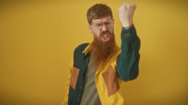Злий рудий бородатий чоловік піднімає кулак на жовтому тлі, зображуючи розчарування. - Фото, зображення