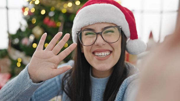 Jeune femme hispanique saluant à la caméra par arbre de Noël faire appel vidéo à la maison - Photo, image