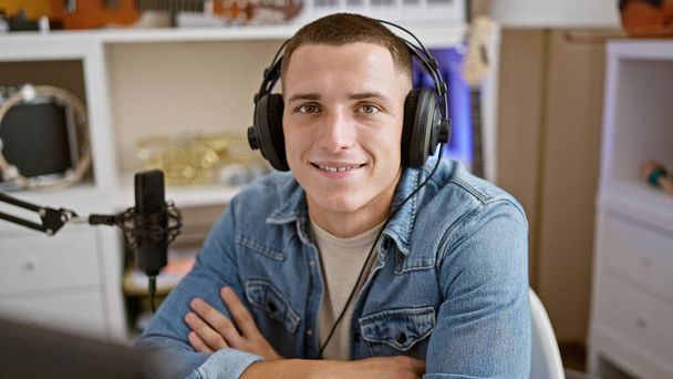 Χαμογελώντας νεαρός άνδρας με ακουστικά σε ένα στούντιο μουσικής, απεικονίζοντας μια φιλόξενη και επαγγελματική ατμόσφαιρα. - Φωτογραφία, εικόνα