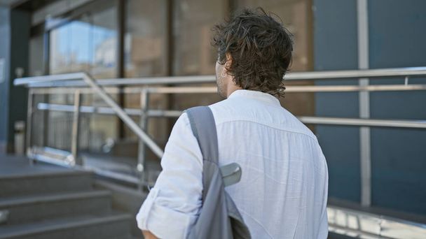 Вид ззаду випадкового іспаномовного чоловіка з рюкзаком, що стоїть на міській вулиці міста. - Фото, зображення