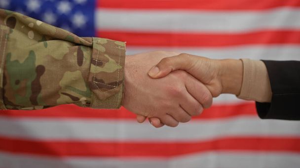 Eine zivile Frau und ein militärischer Mann geben sich vor einer amerikanischen Flagge die Hand und symbolisieren damit die Kollaboration. - Foto, Bild