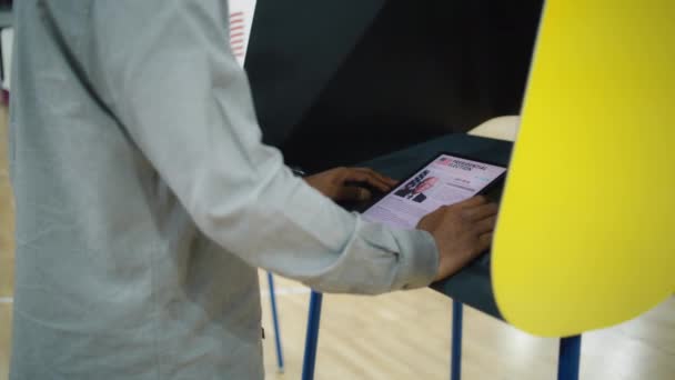 Ciudadano de los Estados Unidos utiliza tableta para votar. Hombre afroamericano, votante masculino hace elección y vota en la cabina de votación en el lugar de votación. Elecciones presidenciales en los Estados Unidos. Deber cívico. - Imágenes, Vídeo