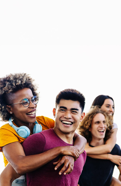 Vertical photo of diverse group of young people having fun together outdoors. Happy multiracial men giving girlfriends piggyback ride. Friendship lifestyle concept. - Photo, Image