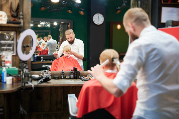 Перукар використовує гребінець і бритву для стрижки волосся. Професійний перукар гоління маленьких дітей поп. - Фото, зображення