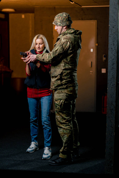 プロの射撃範囲で 軍の男が言う ピストルとの正しい姿勢を女の子に示す - 写真・画像
