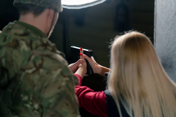 primer plano en un campo de tiro profesional un militar le dice y muestra a una chica la postura correcta con una pistola es - Foto, Imagen