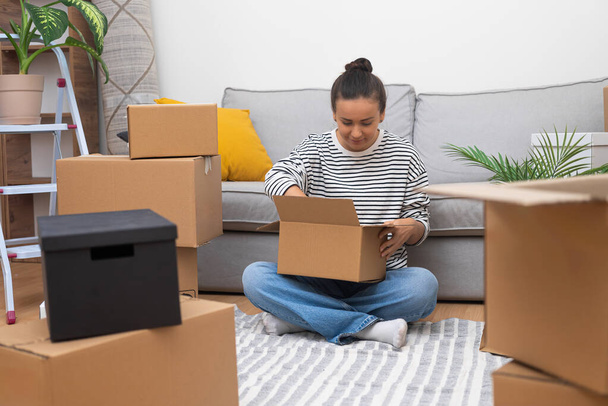 Движение вперед: Молодая женщина в новом доме, окруженная коробками, распаковывает свой мир, представляя переселение, аренду или домовладение - Фото, изображение