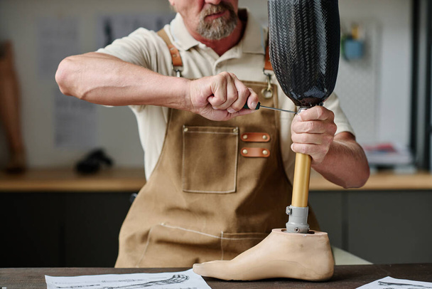 Primer plano del artesano senior construyendo prótesis de piernas personalizadas en el taller, espacio de copia - Foto, imagen