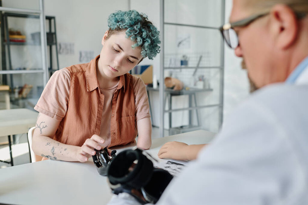 Portret van jonge vrouw met blauw haar adviserende arts in orthologie kliniek tijdens arm prothetische fitting - Foto, afbeelding