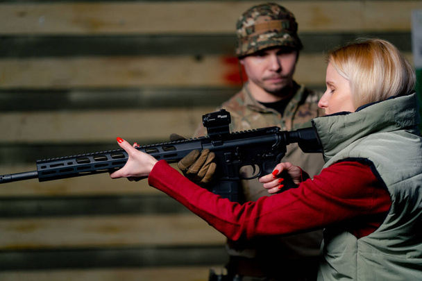 En un campo de tiro profesional, un entrenador militar enseña a una chica barata a sostener correctamente un rifle de la OTAN. - Foto, Imagen