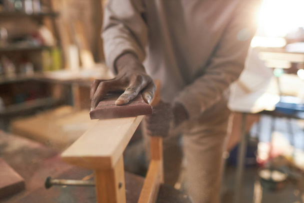 Close-up de artesão preto cuidadosamente lixar móveis de madeira na oficina de carpintaria rústica, espaço de cópia - Foto, Imagem