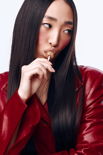 Elegante Frau mit langen schwarzen Haaren und roter Jacke, die Nahrung im Mund hält, Porträt in Nahaufnahme - Foto, Bild