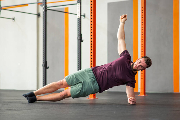 Flexible forte mâle performant côté planche calisthénique exercice sur le sol dans le club de fitness moderne - Photo, image