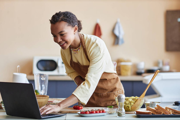 Портрет улыбающейся черной молодой женщины, смотрящей кулинарное видео онлайн на кухне, пространство для копирования - Фото, изображение