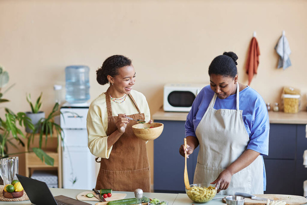 Tailliertes Porträt zweier afroamerikanischer Frauen, die gemeinsam in der gemütlichen Küche kochen und Spaß haben, Kopierraum - Foto, Bild