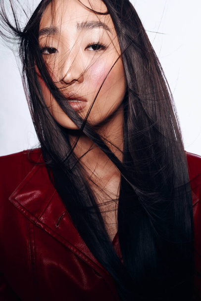 Elegante donna con lunghi capelli neri e giacca di pelle rossa in posa per una foto in ambiente urbano - Foto, immagini